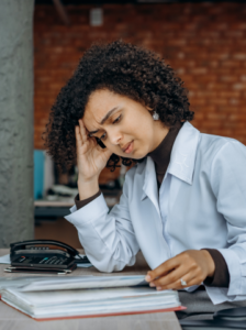 Woman leaning over papers with her hand on her forehead and a distressed look.